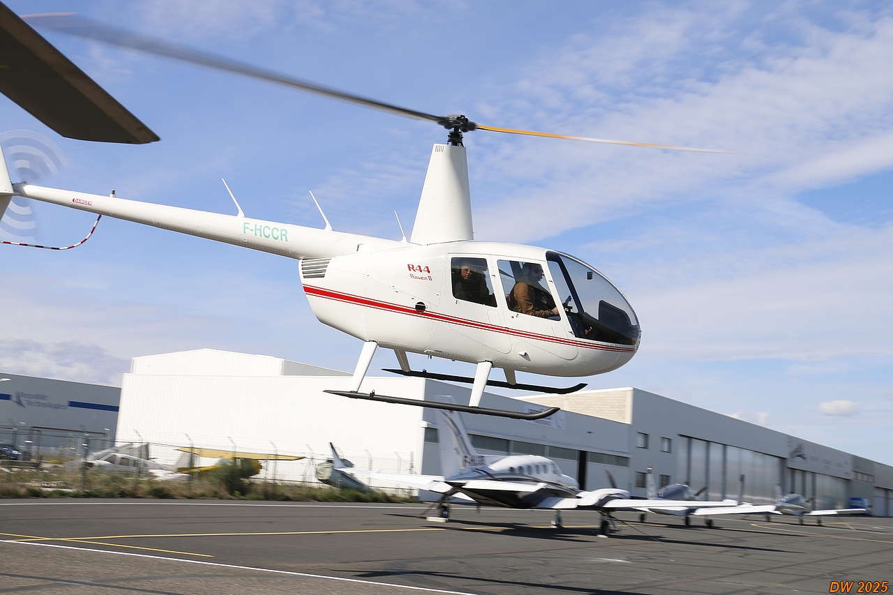 Hélicoptère Robinson R44 en vol au-dessus d'un paysage, illustrant la formation pratique de pilotage.