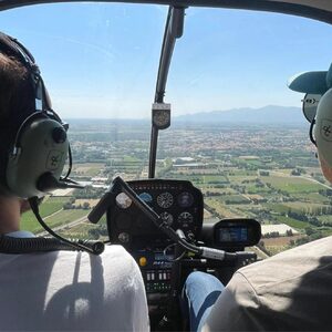Deux personnes pilotent un hélicoptère au-dessus de champs et montagnes avec casques-radio.