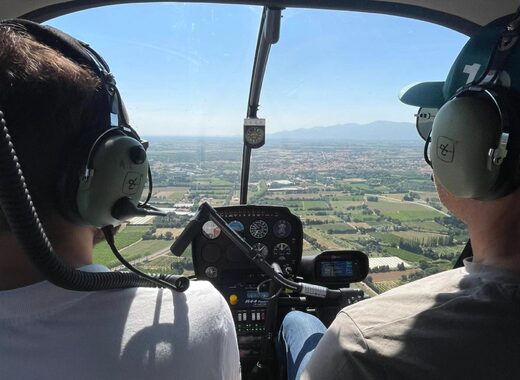 Deux personnes pilotent un hélicoptère au-dessus de champs et montagnes avec casques-radio.