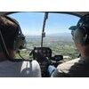 Deux personnes pilotent un hélicoptère au-dessus de champs et montagnes avec casques-radio.