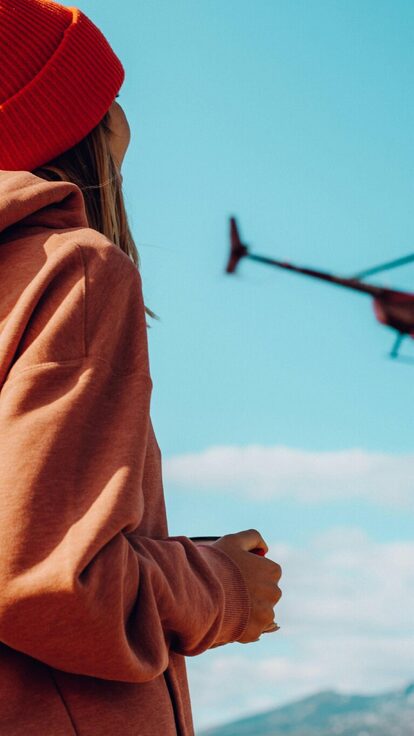 Personne en orange observe un hélicoptère voler au-dessus des montagnes, ciel dégagé.
