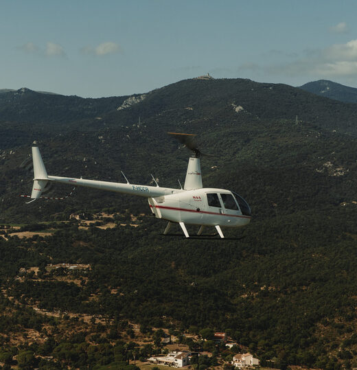 Un hélicoptère blanc survole des montagnes boisées.