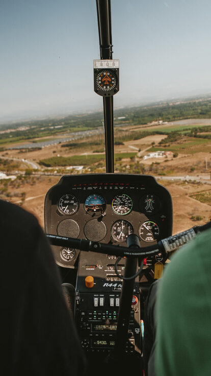 Vue du cockpit d'hélicoptère : deux personnes, paysage visible et instruments de vol.